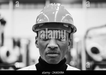 African engineer working inside robotic factory - Focus on face - Black and white editing Stock Photo