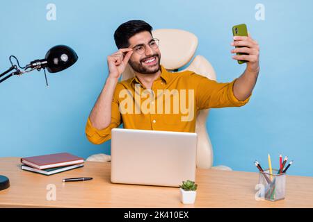 Photo of cheerful person sit chair hand touch eyeglasses make selfie portrait isolated on blue color background Stock Photo