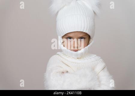 portrait of an angry little girl in a white knitted hat and sweater Stock Photo