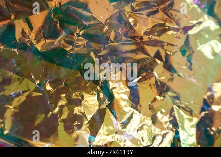 Holographic colored wrinkled yellow foil. Holographic texture of real fabric in yellow tones. Holographic Colorful plastic Film. High quality photo Stock Photo