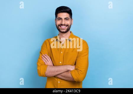 Photo of smart brunet millennial guy crossed arms wear yellow shirt isolated on blue color background Stock Photo