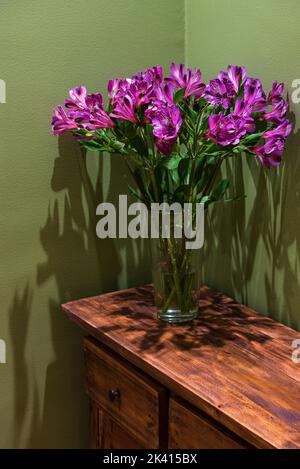 Lily flowers bouquet on vintage wooden chest of drawers in green painted room. Rustic interior ideas concept. Lifestyle background. Stock Photo