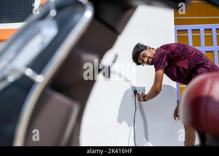 young indain man charging EV or electric scooter battery at charging point - concept of technology, renewable and charging station. Stock Photo