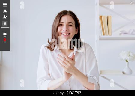 Online education. Happy woman. Screen mockup. Beautiful smiling lady sitting desk clapping hands having virtual chatting in light room interior. Stock Photo
