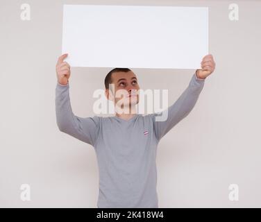 Young man holding a white panel above his head isolated on white background stock photo Stock Photo