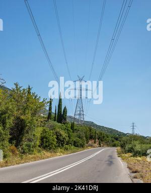 High voltage power lines and pylons over an asphalt road, blue sky background. Metal pole, Electric energy transmission Stock Photo