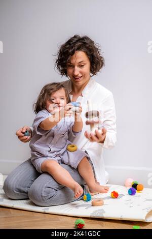 Little baby girl and mommy playing at home sitting on floor, mother and daughter laughing having fun together Stock Photo