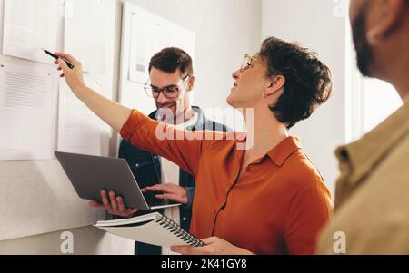 Mature businesswoman discussing some reports with her team during an office meeting. Group of creative businesspeople working on a new strategy in a m Stock Photo