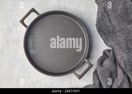 Black cast iron empty frying pan and gray kitchen towel on a gray concrete background Stock Photo