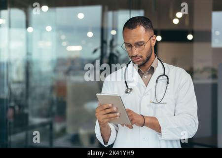 Serious and focused thinking african american doctor using tablet computer, man working inside modern clinic office Stock Photo
