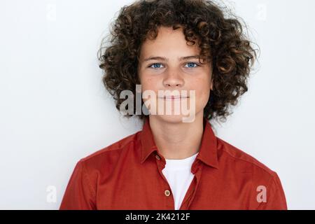 Nice curly boy with blue eyes in red shirt looking at camera, studio shot Stock Photo