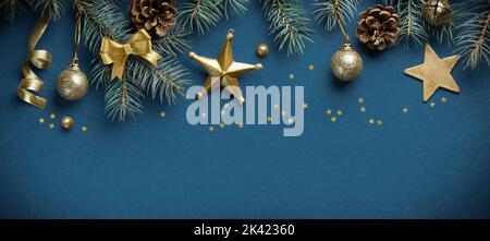 Christmas top border composition made of fir branches, cones and golden stars decorations on blue background. Flat lay, top view, copy space Stock Photo