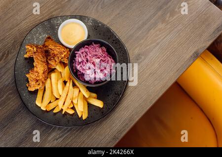 Fried, roast breaded chicken meat, strips with beet root salad, french fries and cheese sauce on black plate on table Stock Photo