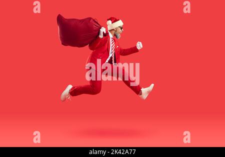 Santa in red suit and hat delivering presents, carrying big sack and running fast Stock Photo