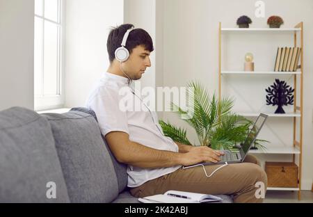 Adult man studying online, sitting on sofa at home and using his laptop computer Stock Photo
