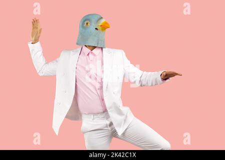 Funny man in rubber pigeon mask and in white formal suit dancing on pink background. Stock Photo