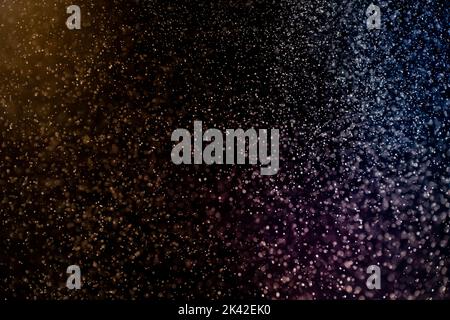 Dust particles floating on a colorful rainbow light on black background. Glittering sparkling flickering overlay. Stock Photo