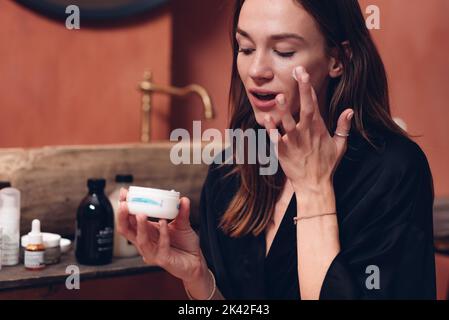 Young woman applying cream on her face. Stock Photo