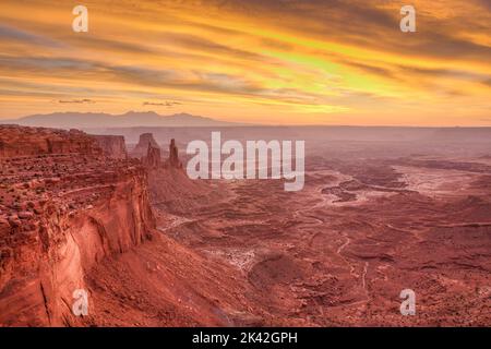 Colorful sunrise over the White Rim in Canyonlands NP, Utah, with Washer Woman Arch, Monster Tower & Airport Tower at left & La Sal Mountains behind. Stock Photo