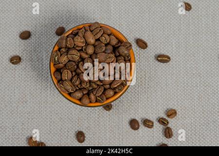 Cup with coffee beans on the background, spilled coffee beans near the cup, top view of coffee. Stock Photo