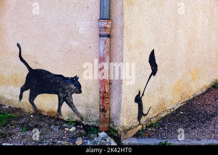 Silhouettes of a mouse ambushing an unsuspecting cat with an axe, painted on te corner of a house in Dun-les-Places, department of Nièvre, France Stock Photo