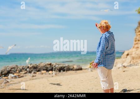 Elderly woman standing on the beach and looking into the distance Stock Photo