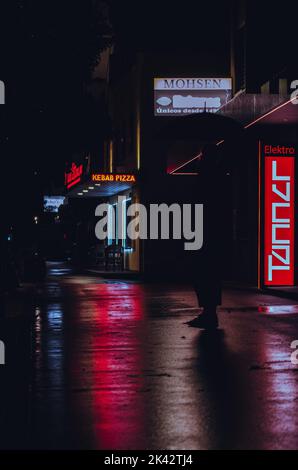 Neon night life on the streets. Bright neon signs reflecting on the wet / rainy street. Neon signs creating silhouette of a person. Stock Photo