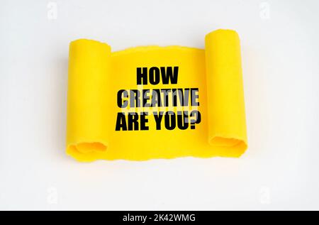 On a white surface, a yellow scroll of paper with the inscription - HOW CREATIVE ARE YOU. Business concept. Stock Photo