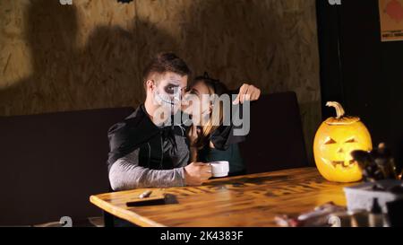 date in style of Halloween party, night, twilight, in the rays of light, guy with a girl dressed in costumes and with a terrible makeup are kissing. High quality photo Stock Photo