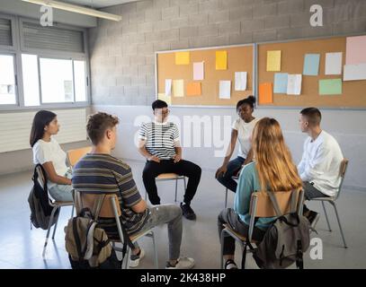 Group of multi-ethnic students sitting in a circle in a classroom while talking about their emotions. Emotional education, assembly, high school Stock Photo