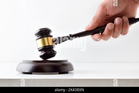 Hand striking on wooden base with judge's mallet on white table and isolated background.  Front view Stock Photo