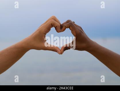 Hands of differents color making heart shape in the sky. Valentine's Day, lovers Stock Photo