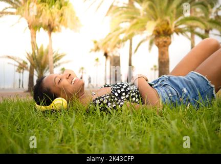 African american woman listening to music lying on the grass in the park  Stock Photo