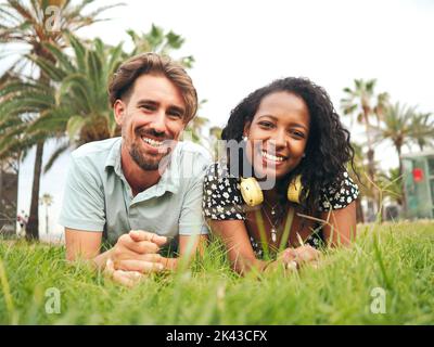 Smiling young multiethnic heterosexual couple lying on the grass in a park  Stock Photo