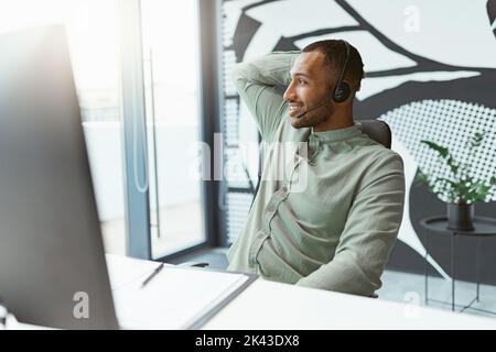 Smiling african businessman working on computer while sitting in modern office and looking at side Stock Photo