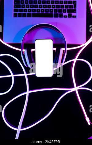 Image of headphones, laptop and smartphone with copy space over neon strands in background Stock Photo