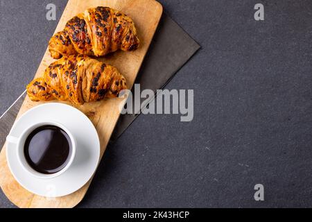 Image of croissants and coffee on wooden board on dark grey surface Stock Photo