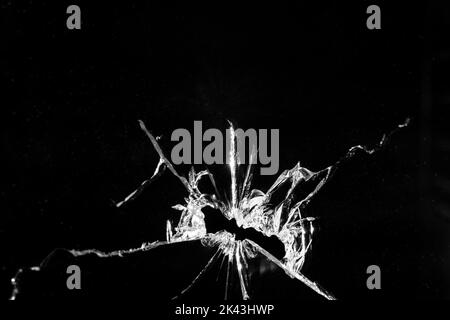 Close up of broken, cracked pane of glass with central hole, on black background with copy space Stock Photo