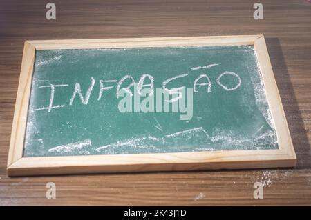 Green chalkboard with the word 'infraction' written in Portuguese with white chalk. Stock Photo