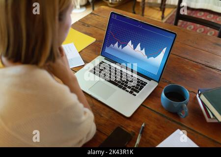 Blond asian businesswoman analyzing graphs over laptop on desk at office Stock Photo
