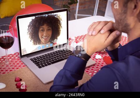 Diverse couple making valentines date video call the woman on laptop screen smiling. online valentines day during quarantine lockdown. Stock Photo