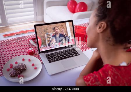 Diverse couple making valentines date video call the man on laptop screen eating. online valentines day during quarantine lockdown. Stock Photo