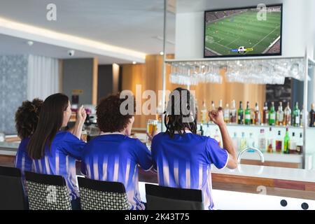 Diverse friends supporting and watching tv in bar with football match ...