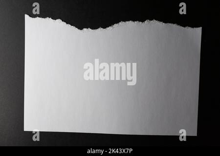 Horizontal sheet of white paper with torn top edge on black background. monochrome light and texture, abstract background image. Stock Photo