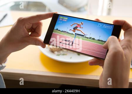Hands of caucasian man at restaurant watching female runner hurdling on smartphone. sports, competition, entertainment and technology concept digital Stock Photo