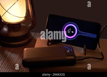 Smartphone with portable power bank energy battery, on book and oil lamp, energy poverty social problem. top view brown background. Stock Photo