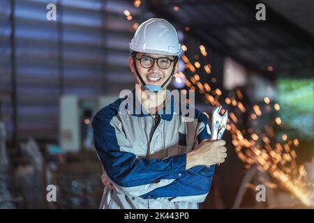 Asian technician smiling young male plumber with pipe wrench standing arms crossed wearing Safety Uniform and hard hat uses tablet checking  Steel or Stock Photo