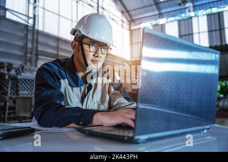 Asian Professional Heavy Industry Engineer Worker Wearing Safety Uniform and hard hat uses computer checking  Steel or Metal Construction Manufacture Stock Photo