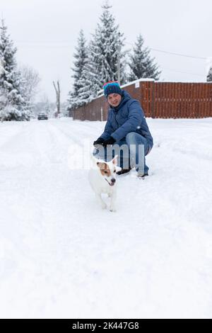 A man and a jack russell terrier play in the snow outside in winter. Vertical photo. Stock Photo