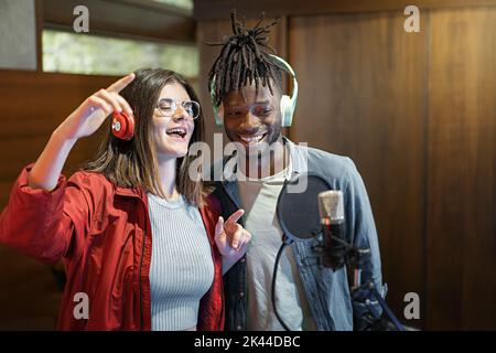 Excited multiethnic couple with microphone and headphones of young broadcasters singing music live and having fun - Social network content creators du Stock Photo